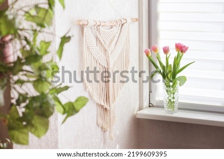 Handmade macrame wallhanging. 100% cotton wall decoration with wooden stick hanging on a white wall.    Female hobby.  ECO friendly modern concept in the interior. 