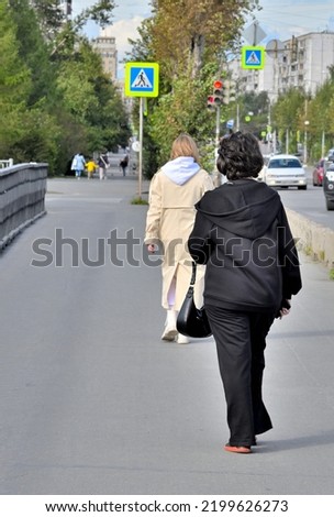 Two women walk along a pedestrian crossing on an autumn day