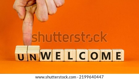 Welcome or unwelcome symbol. Businessman turns wooden cubes and changes the word unwelcome to welcome. Beautiful orange table, orange background. Welcome or unwelcome and business concept. Copy space.