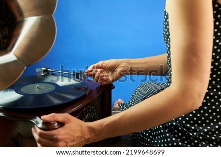A young beautiful woman in black cocktail dress in polka dots puts a pin on the vinyl. Close up view of the hand and vinyl player. The record is playing in the player. Old style concept