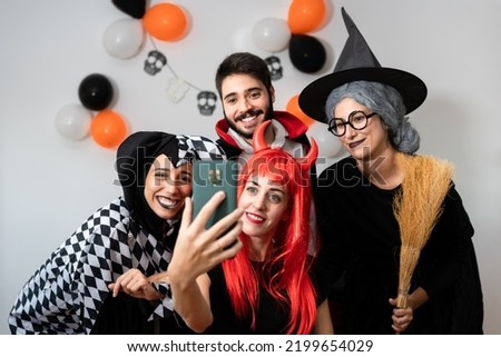 Halloween party at home. Devil, witch, dracula and harlequin posing taking a selfie with their smartphone