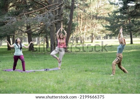 three mature women do yoga outdoors in nature, focus on blonde woman.