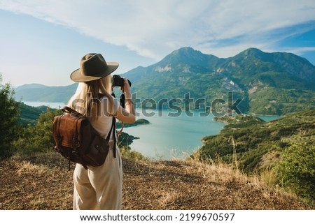 Woman photographer with big backpack taking photo of mountains and blue lake. Travel and hobby concept