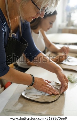 Woman rolling clay, making ceramic plate in studio with floral pattern. Handmade creative work. Pottery workshop for adults. 