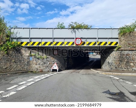 Warning signs on a very low railway bridge with black and yellow hazard stripes and sign displaying 2.3 metre clearance.