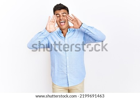 Young hispanic man wearing business shirt standing over isolated background smiling cheerful playing peek a boo with hands showing face. surprised and exited 