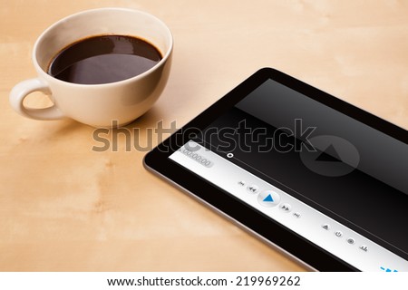 Workplace with tablet pc showing media player and a cup of coffee on a wooden work table close-up