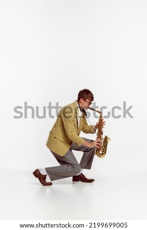 Portrait of young man in stylish yellow jacket playing saxophone isolated over white background. Expressive music. Concept of live music, performance, retro style, creativity, artistic lifestyle Royalty-Free Stock Photo #2199699005