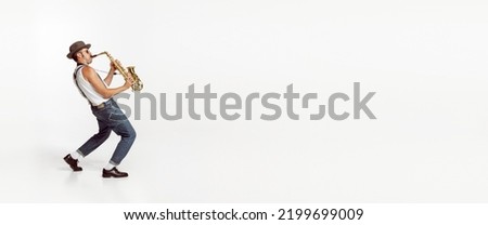 Portrait of stylish man in hat and suglasses playing saxophone , performing isolated over white background. Flyer. Concept of live music, performance, retro style, creativity, artistic lifestyle Royalty-Free Stock Photo #2199699009