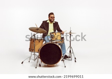 Portrait of stylish brutal man in jacket and sunglasses playing drums isolated over white background. Concept of live music, performance, retro style, creativity, artistic lifestyle Royalty-Free Stock Photo #2199699011