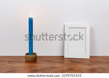 Minimalist still life of a customizable picture frame and blue lit candle. Wood and white background