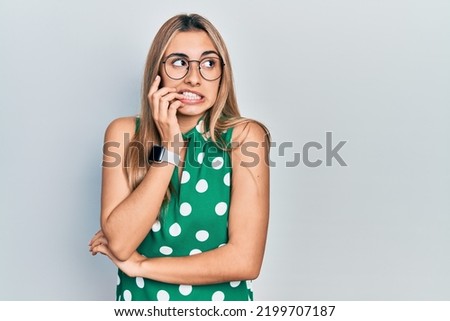 Beautiful hispanic woman wearing elegant shirt and glasses looking stressed and nervous with hands on mouth biting nails. anxiety problem.  Royalty-Free Stock Photo #2199707187
