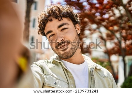Handsome hispanic man with beard smiling happy outdoors on a sunny day taking a selfie photo