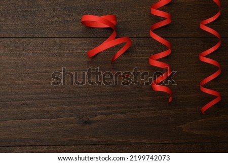 Red serpentine streamers on wooden table, flat lay. Space for text