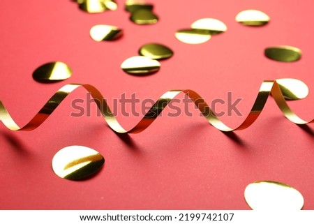 Shiny golden serpentine streamer and confetti on red background, closeup