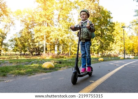 Profile view portrait of cute blond little caucasian school girl wear helmet enjoy having fun riding electric scooter city street park outdoors on sunny day. Healthy sport children activities outside Royalty-Free Stock Photo #2199755315