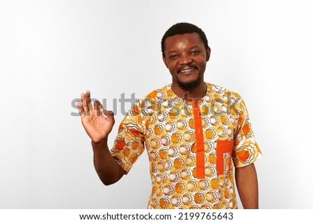 Smiling black man with OK hand gesture in African bright clothes isolated on white background, casual African wear. Nice bearded black guy portrait with excited funny emotions