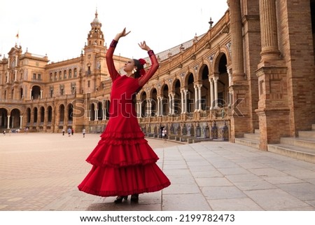 Beautiful teenage woman dancing flamenco in a square in Seville, Spain. She wears a red dress with ruffles and dances flamenco with a lot of art. Flamenco cultural heritage of humanity. Royalty-Free Stock Photo #2199782473