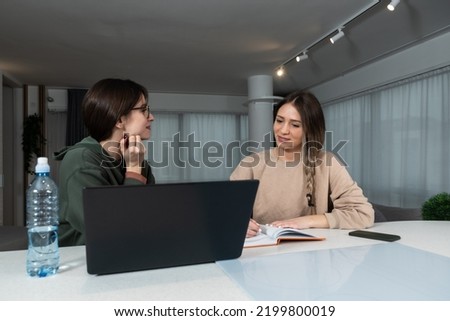 Two young college students study together helping each other with lection for exam. Roommates doing homework together in their apartment, reading and searching the internet for answers. Education 
