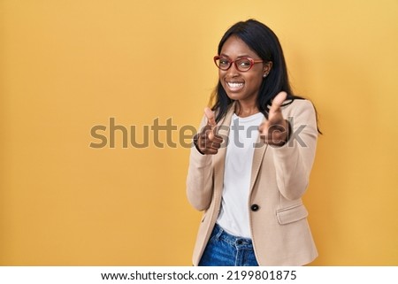 African young woman wearing glasses pointing fingers to camera with happy and funny face. good energy and vibes. 