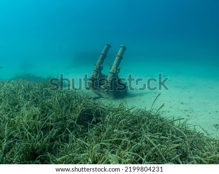 Antique cannons on a sandy sea floor. Beautiful turquoise water in the background