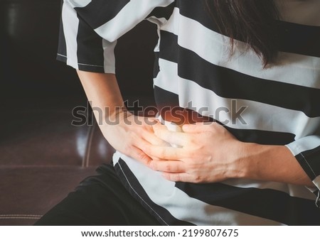 Asian woman her is suffering from stomach pain in the right side with hands feeling acute pain. Stomach-ache concept. Royalty-Free Stock Photo #2199807675