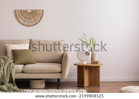 Minimalist composition of elegant and outstanding space with beige sofa, coffee table, vase, green plaid and sculpture. Beige wall. Home decor. Template. 