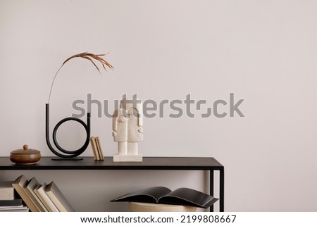 The stylish composition of minimalistic interior with copy space.  Black commode, vase with dried flowers, sculpture and personal accessories. Beige wall. Home decor. Template.  Royalty-Free Stock Photo #2199808667