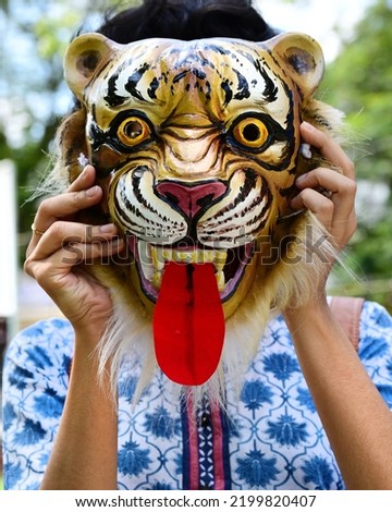 Girl wearing a mask, depicting a snarling tiger, which she borrowed from a performer for taking the picture.