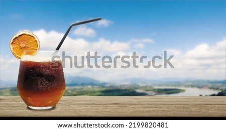 Ice lemon tea drink on wooden bar with blured natural landscape mountain, river and sky view, that make refreshing in the morning vacation day