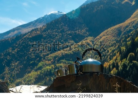 Close-up of a metal teapot and two cups on a stone against the background of mountains on a sunny day, copy the space. Beautiful, atmospheric autumn landscape of picnic mountains