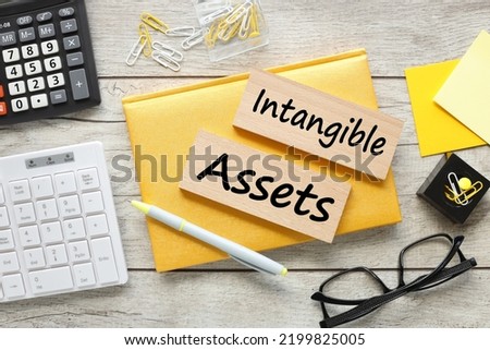 Intangible assets. two wooden blocks on a yellow notepad with text near glasses Royalty-Free Stock Photo #2199825005