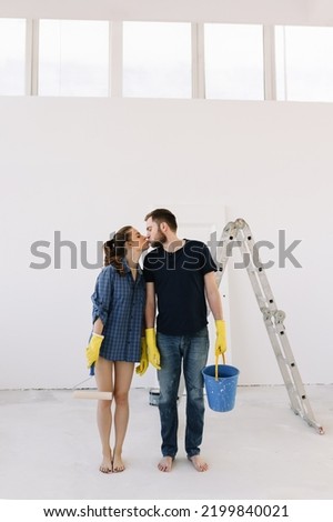Couple in love, newlyweds in protective glasses and gloves are making repairs in an empty room, painting white walls and updating the interior.  Man and a woman moved into a new house. Selective focus