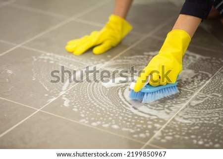 Woman's hand wearing yellow rubber gloves using a brush to scrub the tile floor, housewife, housework, housekeeping job, professional female janitor cleaning Royalty-Free Stock Photo #2199850967