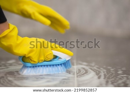 Close-up of a woman's hand using a brush to scrub the tile floor while donning yellow rubber gloves; housewife, housework; cleaning service Royalty-Free Stock Photo #2199852857