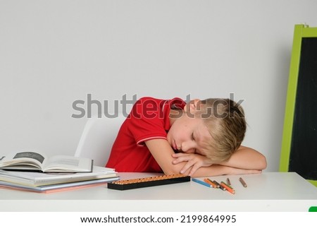 Little boy feeling tired bored and sleepy doing school homework at the table.