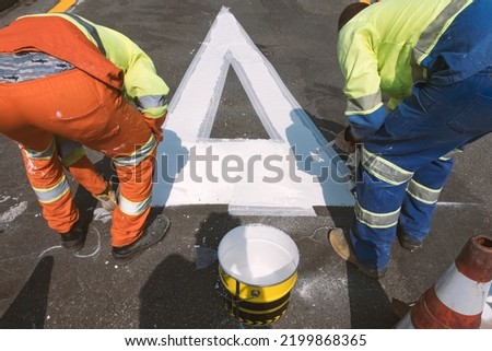 Traffic signage. Asphalt painting. Workers painting the floor. Preference sign at the intersection.