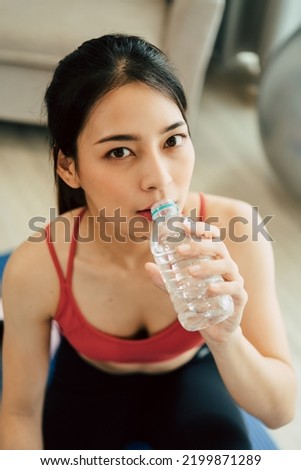 Asian woman in yoga sportswear sitting on the mat and drinking water.