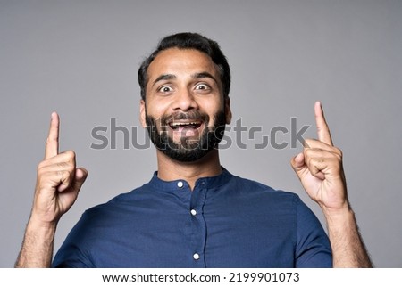Happy surprised indian business man looking at camera pointing finger up hand gesture indicating advertising new product promotion, presenting great online offer ad standing isolated on gray. Portrait Royalty-Free Stock Photo #2199901073
