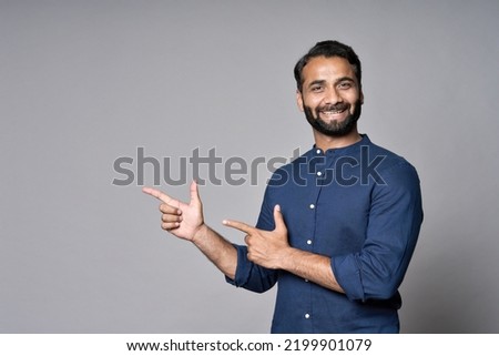 Happy indian business man salesman looking pointing fingers hand gesture aside indicating advertising recommending new commercial promotion, presenting sale offer standing isolated on gray background. Royalty-Free Stock Photo #2199901079