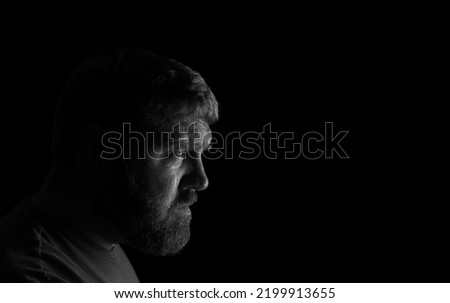 Caucasian male site alone in a room with a tear running down his cheek.