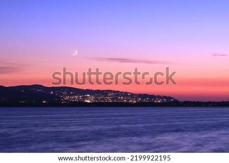 Porto Santo Stefano by night, as seen from Orbetello across the lagoon, at sunset, with great colors and a nice moon in the sky. Romantic photo of italian summer holidays. Long exposure photography.
