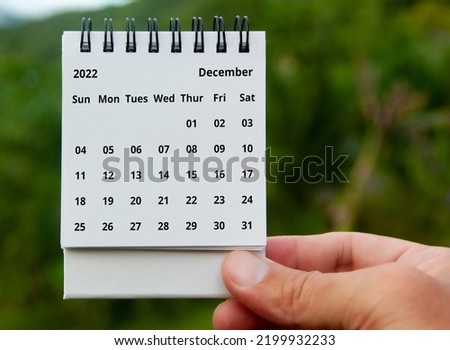 Hand holding December 2022 calendar with copy space and nature background. Royalty-Free Stock Photo #2199932233