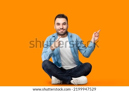 A picture of a handsome Arab young man sitting on the ground pointing with his hands to the side, a picture of a promotional advertisement or design with an orange background