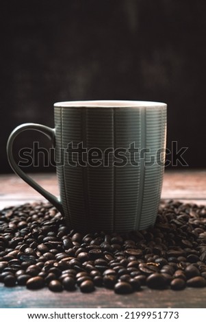 A mug of coffee in a pile of coffee beans on wooden table with black background