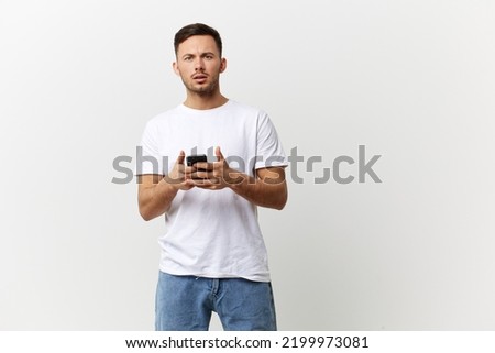 Confused unhappy tanned handsome man in basic t-shirt get shock info from phone message posing isolated on over white studio background. Copy space Banner Mockup. Distance online communication concept
