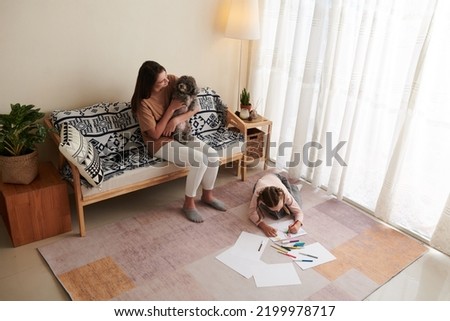 Young woman playing with dog when her daughter drawing pictures on floor