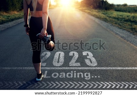 Sporty girl who is at the starting line to pass in 2023 year and the Loading bar drawn on asphalt. Concept of new professional achievements in the new year 2023 and success. Royalty-Free Stock Photo #2199992827