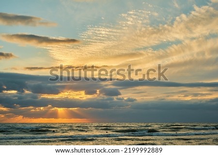Sunset sky over the sea, late evening with colorful clouds of orange sunlight, the rays of the sun shine through the clouds