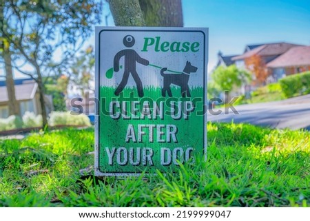 Please Clean Up After Your Dog sign at a neighborhood in San Francisco. Close up view of a pet signage against tree, road, houses and blue sky on a sunny day.